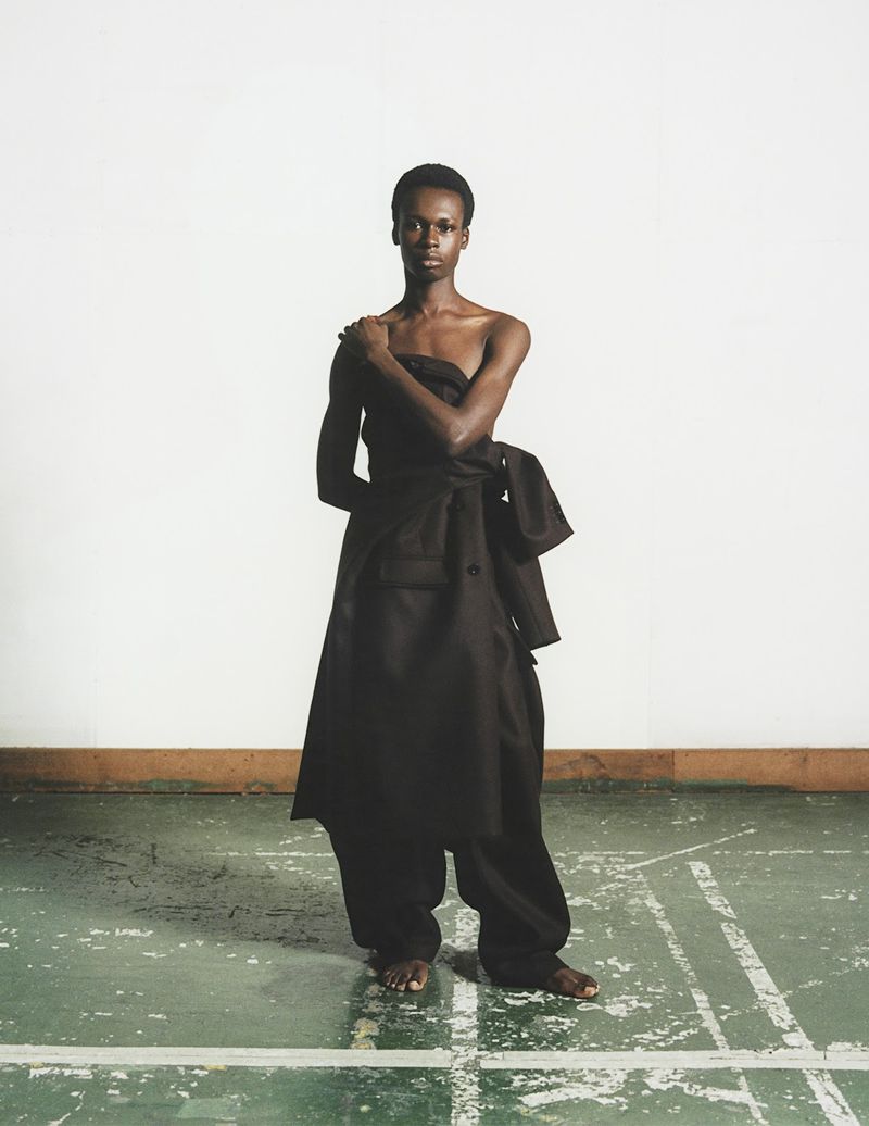 African woman wearing oversized black clothing in a minimalist studio. Fashion editorial shot with natural light and a white backdrop.