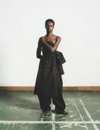 African woman wearing oversized black clothing in a minimalist studio. Fashion editorial shot with natural light and a white backdrop.