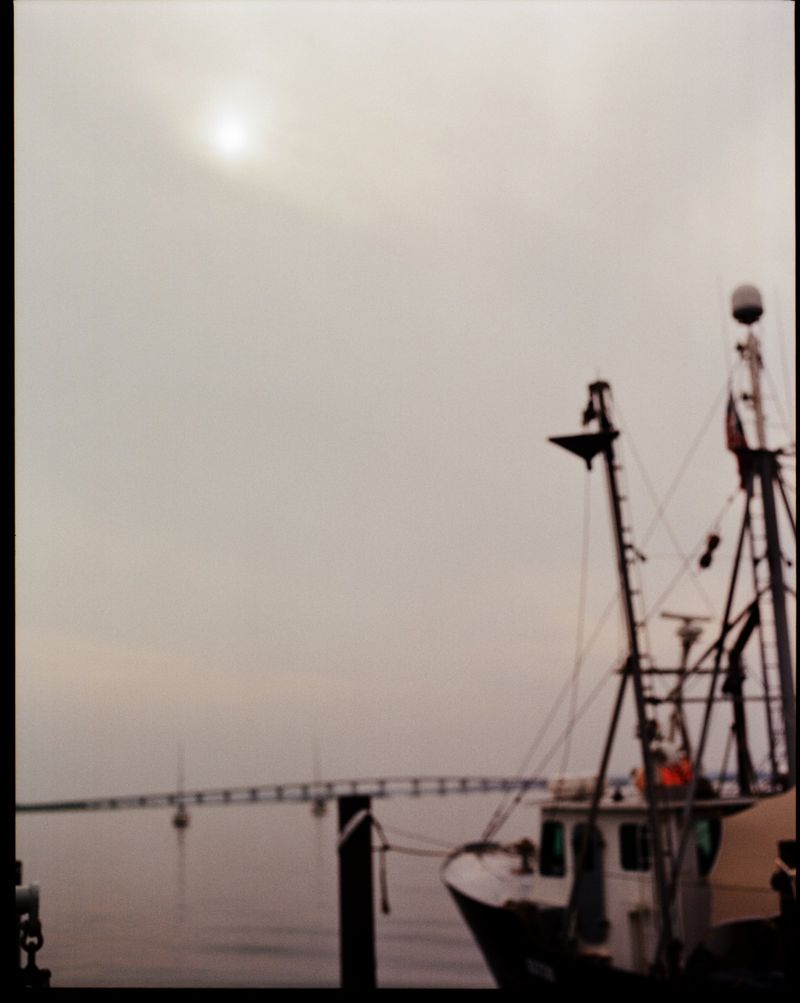Blurred view of a fishing boat docked near a pier under an overcast sky, showing the boat's equipment and the pier in the background.