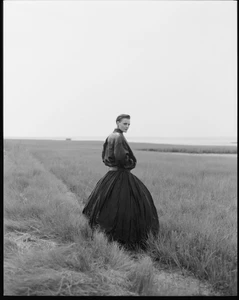 Model Guinevere van Seenus in a dark voluminous skirt standing in an open field for V Magazine