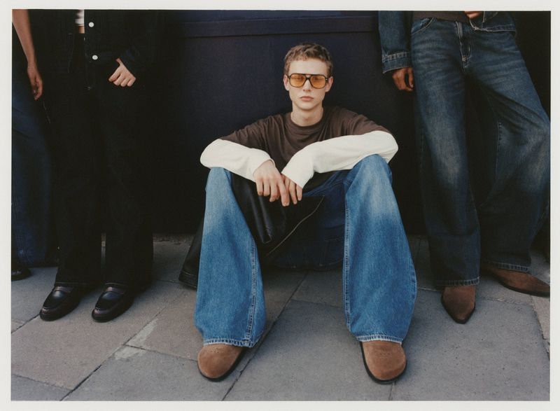 Three people modeling denim jeans and casual tops in a full shot, set against a dark grey background, showcasing fashion and style.