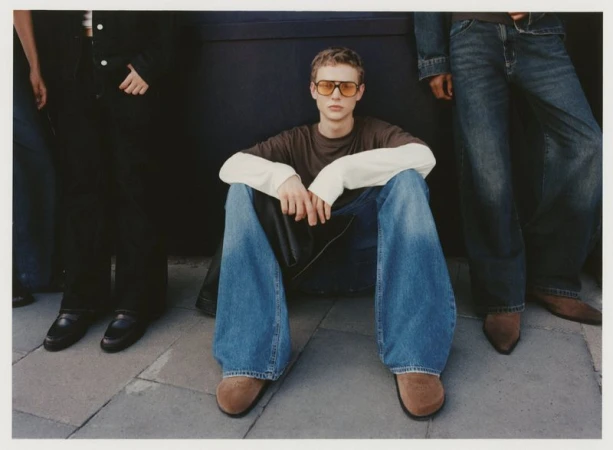 Three people modeling denim jeans and casual tops in a full shot, set against a dark grey background, showcasing fashion and style.