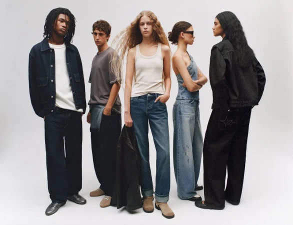 Group of five diverse young adult models wearing denim in a bright studio setting. Fashion-forward clothing, neutral backdrop, and full body shot.