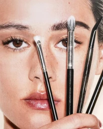 Close-up beauty shot of a model holding makeup brushes in front of her face for Harper's Bazaar France Bazaar Beaute editorial.