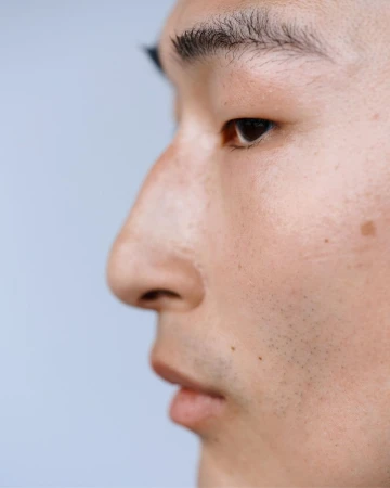 Close-up studio portrait of a fair-skinned adult male of Asian descent in profile, with a neutral facial expression against a light background.
