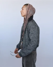 Profile view of Sang Woo Kim wearing a grey tweed jacket and hoodie holding glasses against a white backdrop for Fantastic Man.