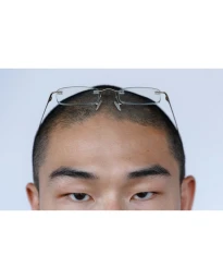 Close-up portrait of a man with a buzz cut wearing rimless eyeglasses perched on his forehead against a pale background