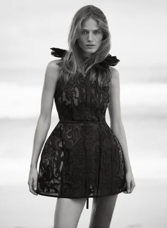 Black and white portrait of a fair-skinned young adult woman wearing a dark short dress with a frilled collar against a neutral background.