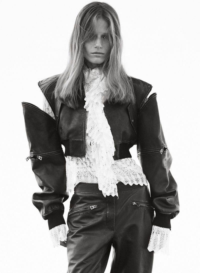 A slender model poses in an outdoor fashion shot, wearing a black leather jacket and pants with a frilly white lace blouse.