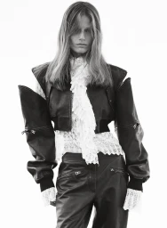 Model in black leather jacket and pants with white lace ruffled blouse against a plain background