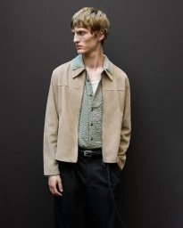 Model wearing a beige suede jacket, sage patterned shirt, and black trousers against a dark background.