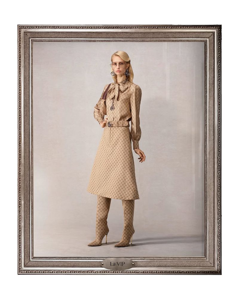 Woman in patterned tan outfit and boots posing in front of a neutral backdrop framed by an ornate silver picture frame for a fashion shoot.