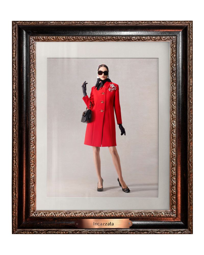Framed fashion photograph of a woman in a red coat, black accessories, and sunglasses, standing against a neutral backdrop.