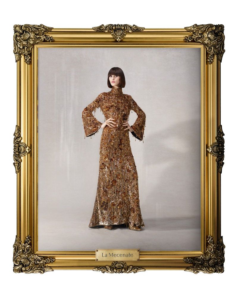 Woman in beaded, vintage-inspired dress with bell sleeves poses in a gold ornate frame against a grey background. Fashion photography.