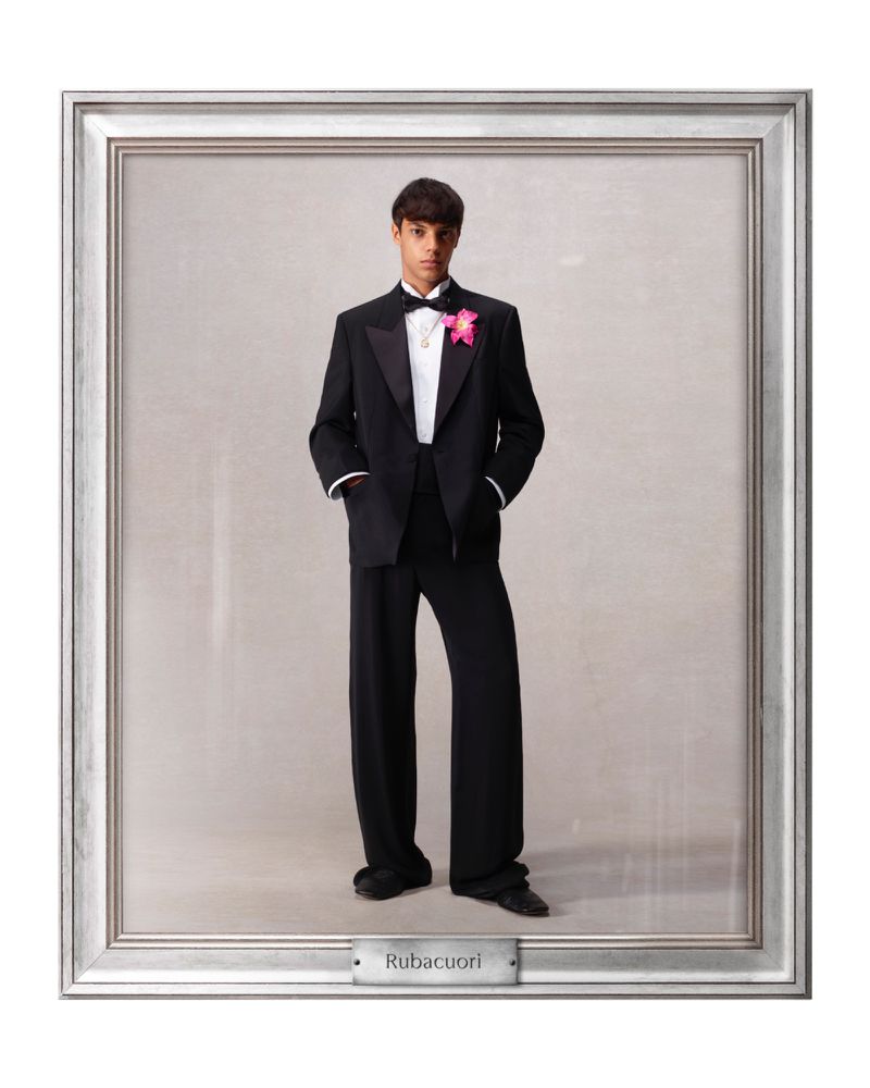 Young man in a formal black tuxedo with a pink corsage stands in a silver picture frame with a gray background and a nameplate.
