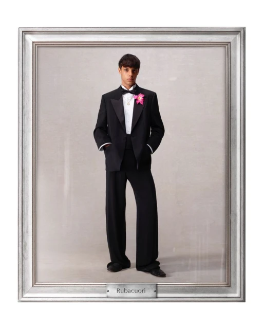 Young man in a formal black tuxedo with a pink corsage stands in a silver picture frame with a gray background and a nameplate.