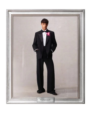 Young man in a formal black tuxedo with a pink corsage stands in a silver picture frame with a gray background and a nameplate.
