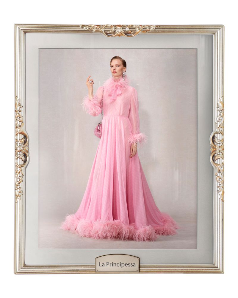 Woman in a pink feathered gown posing inside an ornate silver frame against a light background. Fashion shot, studio lighting.