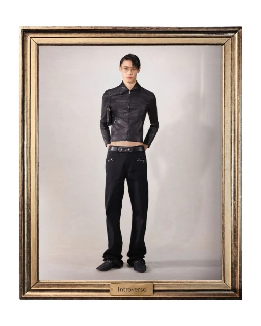 Full-length studio shot of an adult Asian male model in a black jacket and black trousers posing in a gold picture frame against a grey backdrop.