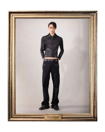 Full-length studio shot of an adult Asian male model in a black jacket and black trousers posing in a gold picture frame against a grey backdrop.