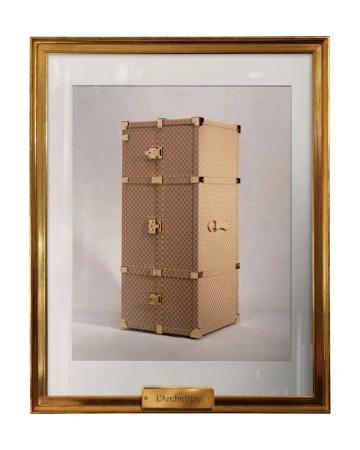 Framed photograph of a stacked set of tan and brown luggage with gold hardware and frame, indoors under studio lighting.