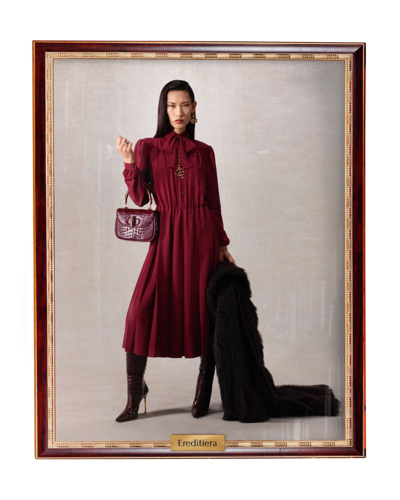 Fashion shot of an Asian woman in a burgundy dress and boots, holding a purse and black coat, framed as a painting.
