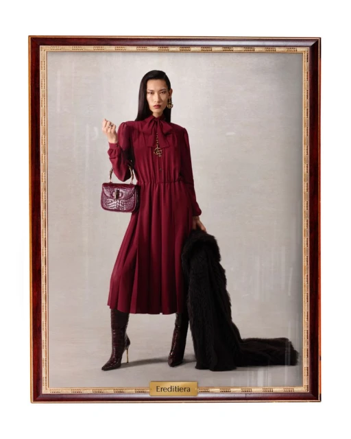 Fashion shot of an Asian woman in a burgundy dress and boots, holding a purse and black coat, framed as a painting.