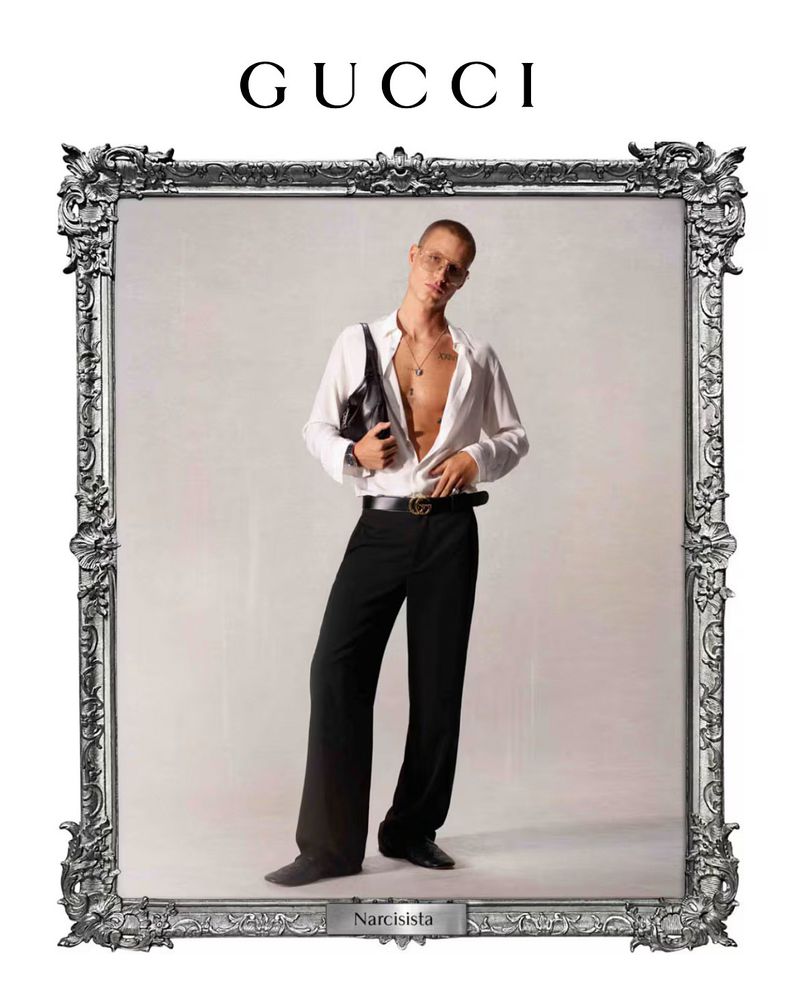 Fashion shot: Person in unbuttoned shirt, dark pants, and Gucci belt posing in decorative silver frame against neutral background.