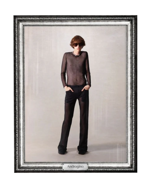 A model in a mesh top and trousers poses in a studio, framed for a fashion editorial. The composition features a neutral backdrop.