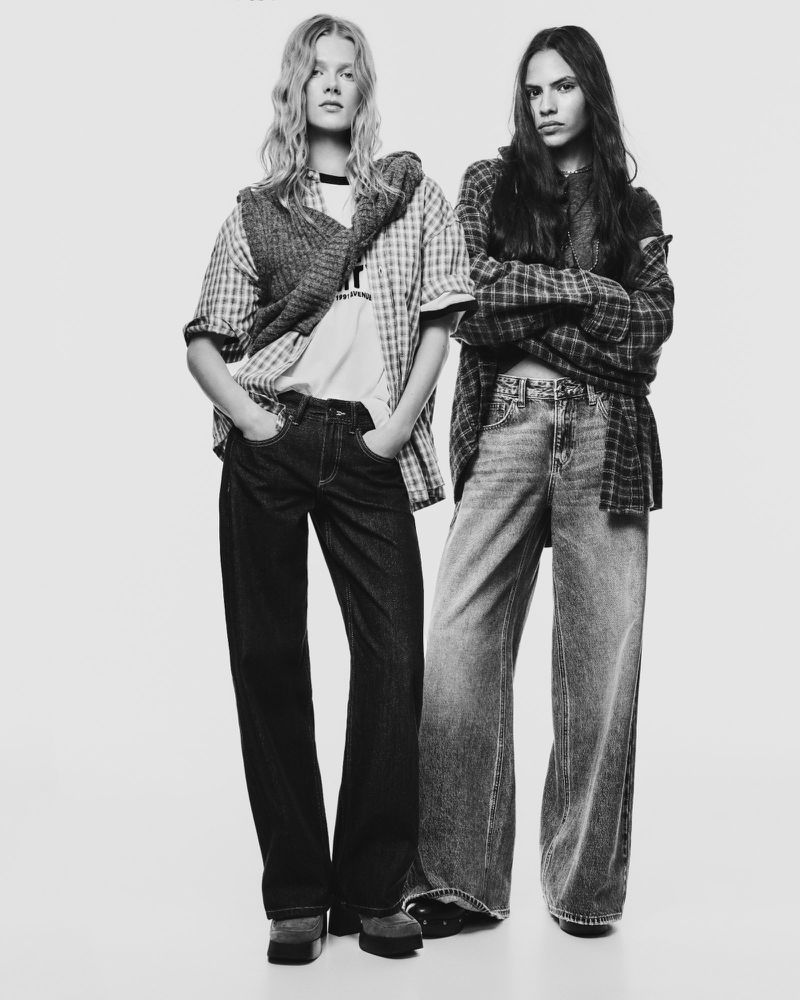 Two fashion models pose in a black and white studio shot, wearing casual outfits with jeans and plaid shirts, showcasing a vintage style.