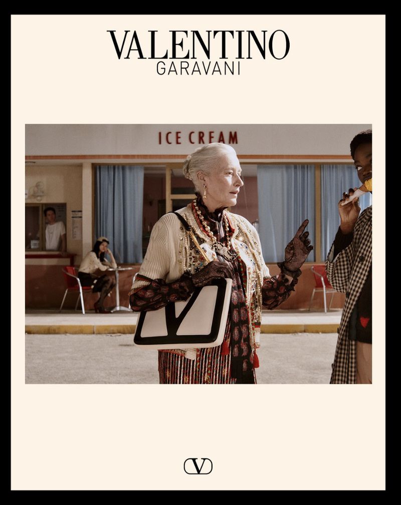 Valentino Garavani fashion scene with senior female model, patterned cardigan, purse with V logo, and ice cream parlor background.