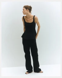 Model Valerie Scherzinger in a black scoop-neck top and black trousers against a white studio background.