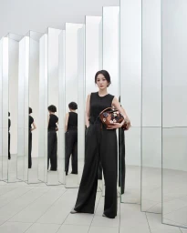 Yang Mi in a black sleeveless jumpsuit holding an embellished floral Loewe Puzzle handbag among vertical mirrored pillars.