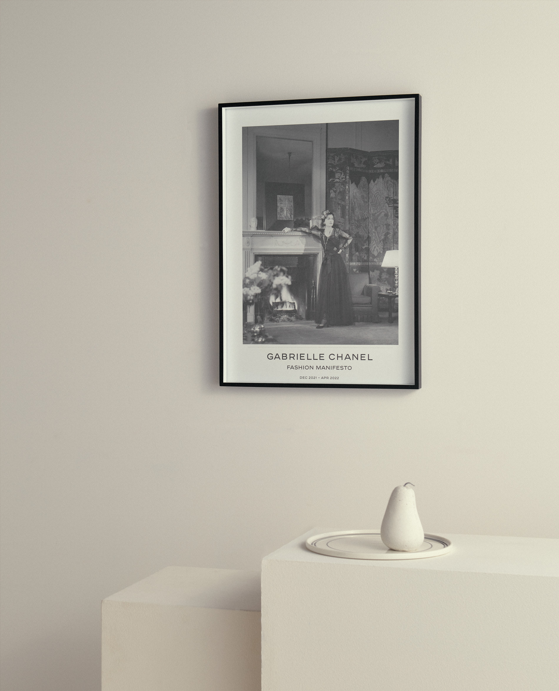 Framed black and white poster featuring a woman in a dress leaning against a fireplace, displayed above a modern white table with vase.