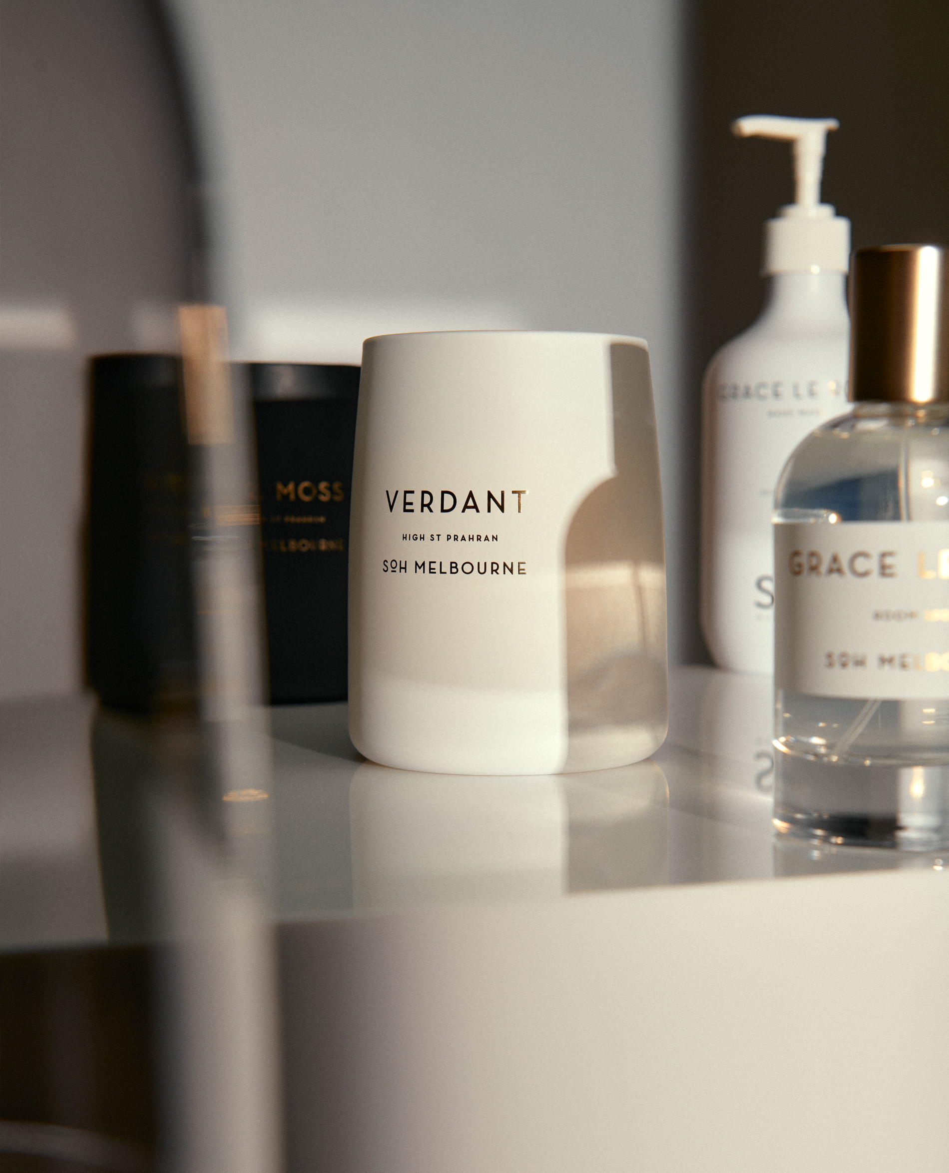 Close-up shot of luxury home fragrances on a reflective surface, including candles and perfume bottles in neutral, sophisticated tones.