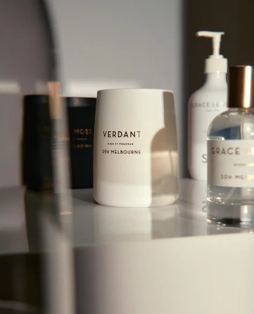 Close-up shot of luxury home fragrances on a reflective surface, including candles and perfume bottles in neutral, sophisticated tones.