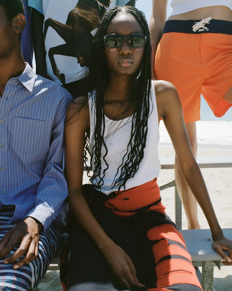 Diverse group of people in fashionable summer clothing sitting outdoors on a sunny day near the beach.