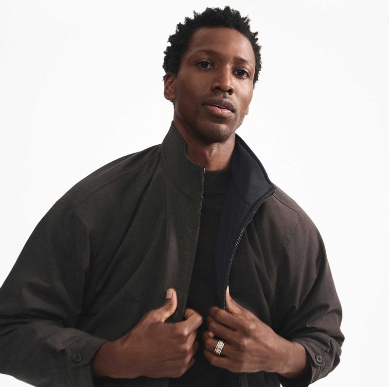 Portrait of an African-American adult male indoors. He wears a dark jacket and a black top, gazing slightly off-center on a light background.