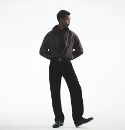 Calvin Royal III standing in a brown zipped jacket, black trousers, and black dress shoes against a white studio background.