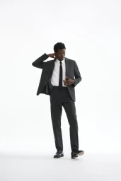 Calvin Royal III poses in a dark tailored suit, white dress shirt, and black necktie against a plain white studio background.