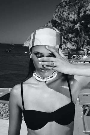 Black and white portrait of a woman wearing a patterned headscarf and a chunky chain necklace outdoors by water