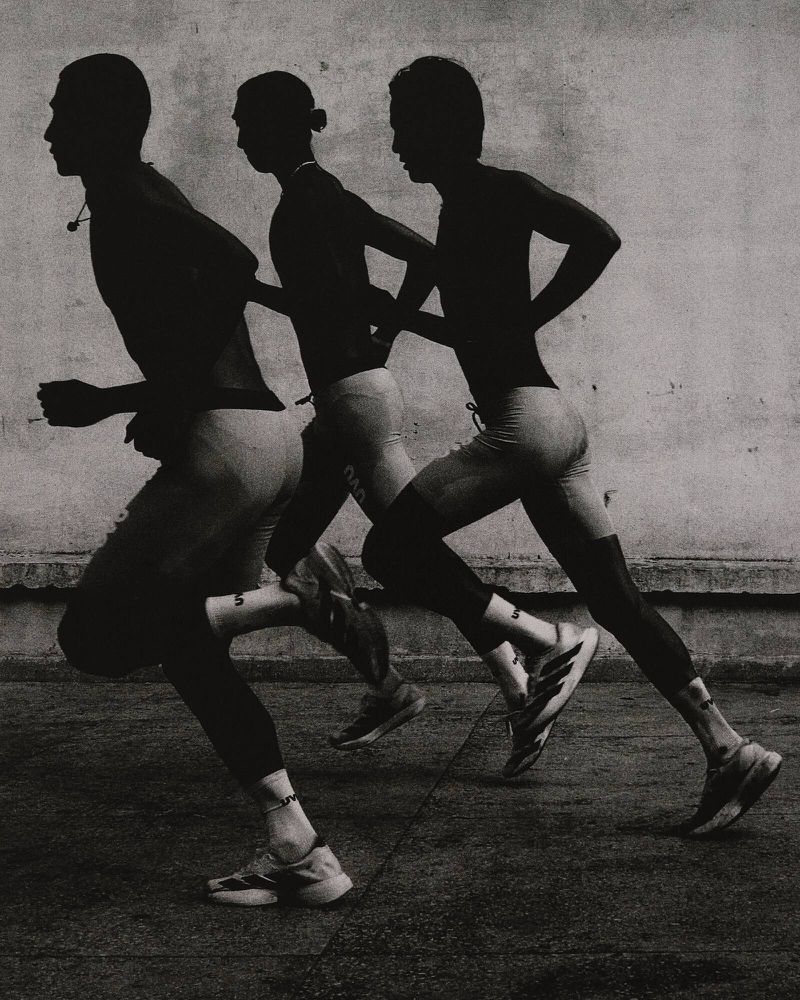 Monochromatic shot of three male runners in motion, captured in silhouette against a textured wall, showcasing athletic physique and form.