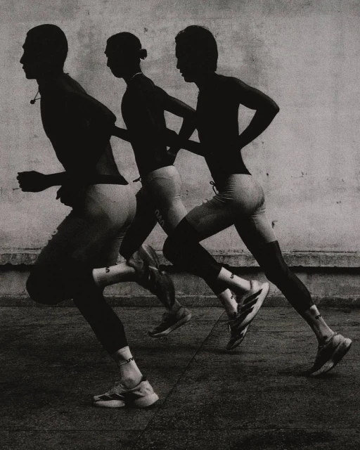 Monochromatic shot of three male runners in motion, captured in silhouette against a textured wall, showcasing athletic physique and form.