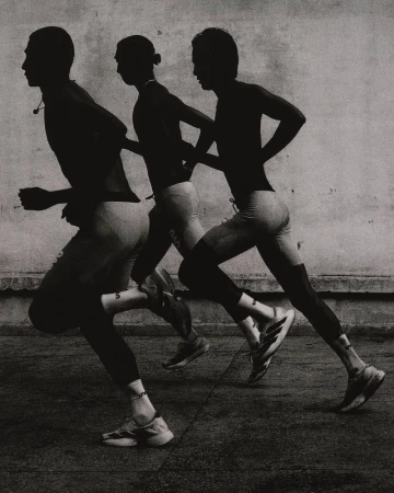 Monochromatic shot of three male runners in motion, captured in silhouette against a textured wall, showcasing athletic physique and form.