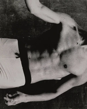 Black and white photograph of a shirtless man wearing athletic shorts with a dark elastic waistband against a textured dark surface.