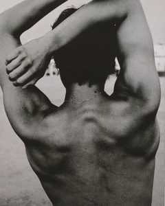 Monochrome rear view of a man with arms raised and clasped behind his head, highlighting back musculature.