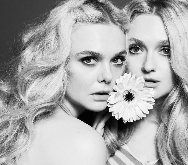 Black and white portrait of two women with blonde wavy hair, holding a white gerbera daisy, photographed in a photo studio.