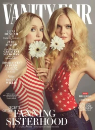 Dakota Fanning and Elle Fanning pose together holding white gerbera daisies on a magazine cover against a grey studio backdrop.