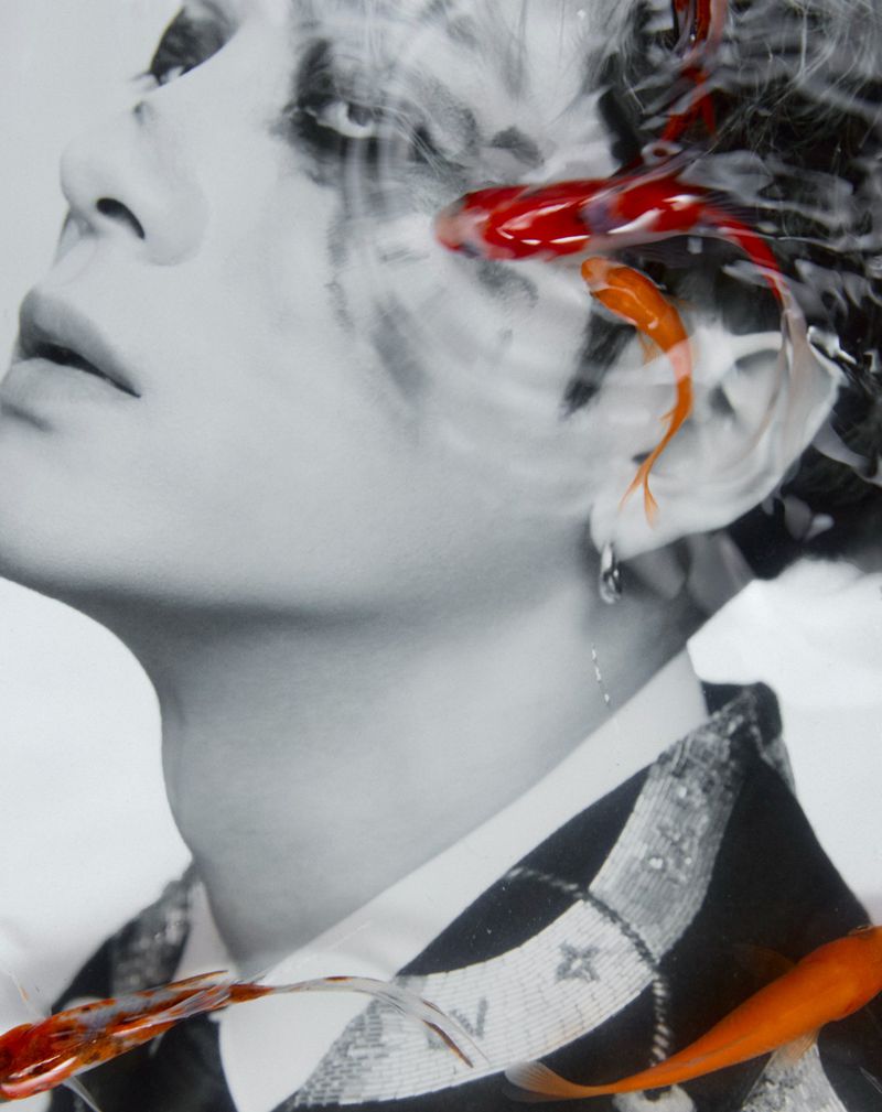 Artistic grayscale portrait of a person overlaid with swimming goldfish and water ripples, creating a surreal aquatic aesthetic.