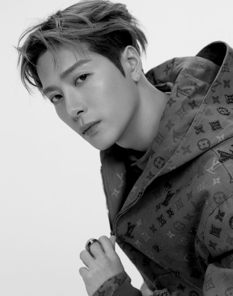 Monochrome portrait of a stylish Asian man in a patterned hooded jacket, showcasing a contemplative expression against a light backdrop.